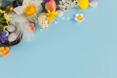 Yuvadaki zarif Paskalya yumurtaları, renkli çiçekler ve kiraz çiçekleri fotokopi alanı ile mavi arka planda yatıyordu. Mutlu Paskalyalar! Tebrik kartı şablonu. Modern bayram afişi. Kutlama bileşimi
