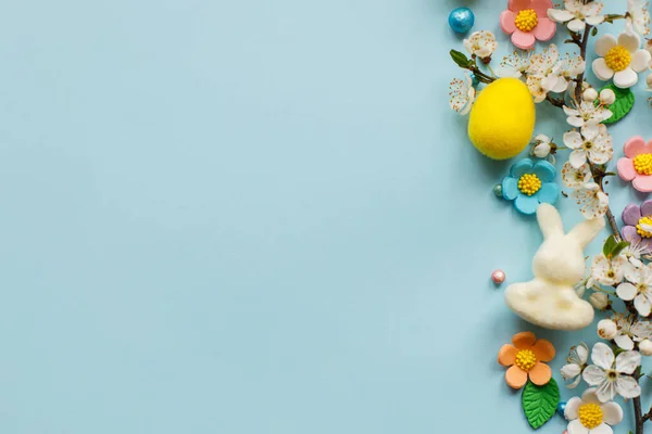 复活节快乐 复活节彩蛋 糖果花 兔子和盛开的樱桃枝平铺在蓝色的背景上 时尚的节日模板 带有文字空间 贺卡或横幅 — 图库照片