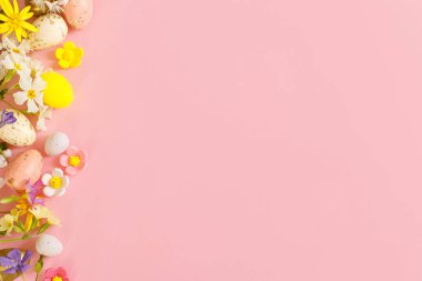 Happy Easter! Easter flat lay with stylish eggs and blooming spring flowers on pink background. Modern template with space for text. Greeting card or banner. Festive border