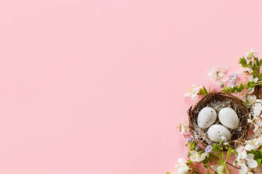 Happy Easter! Easter flat lay with stylish eggs in nest and blooming cherry branch on pink background. Modern template with space for text. Greeting card or spring banner