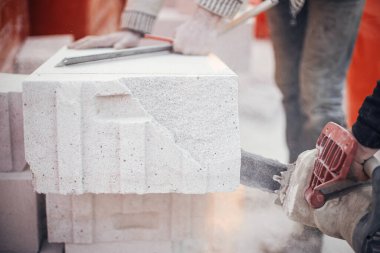 Otoklavize edilmiş beton bloğu elektrikli testereyle kesen işçiler. İnşaatçılar duvarcılık için beyaz blokları kesiyorlar. İnşaat alanındaki ev inşaatı.