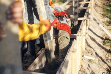 Workers pouring concrete in formwork for foundation. Construction site, process of house building. Builders pouring concrete with pump truck in wooden formwork with reinforcement