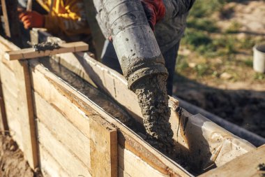 Workers pouring concrete in formwork for foundation. Construction site, process of house building. Builders pouring concrete with pump truck in wooden formwork with reinforcement