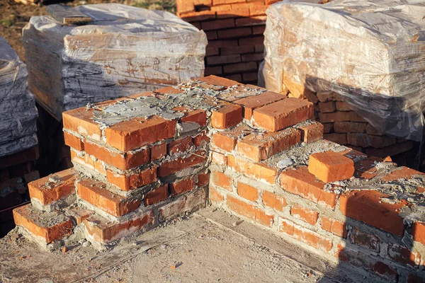 Bricks masonry with cement on concrete foundation, process of house building. Red bricks for laying on concrete foundation. Building materials at construction site