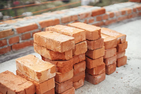 Stack of red bricks on concrete foundation, process of house building. Concrete foundation with bricks for laying. Building materials at construction site