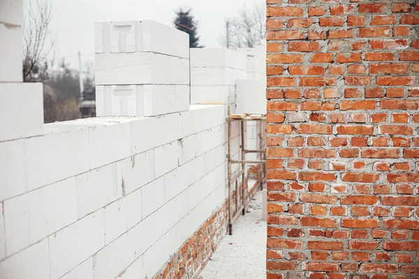 Masonry autoclaved aerated concrete blocks and bricks on concrete foundation. Laying walls with white blocks. Process of house building at construction site