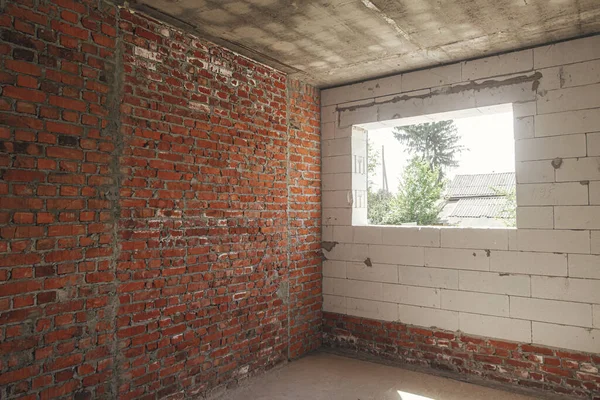Unfinished house inside. Aerated concrete blocks and brick walls with windows, doorways and concrete floor. Process of house building at construction site. New house construction