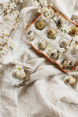 Happy Easter! Rustic easter flat lay. Stylish easter eggs and blooming spring flowers on rustic table. Natural quail eggs in tray, feathers and cherry blossoms linen fabric.
