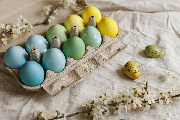 Happy Easter! Rustic easter still life. Natural painted eggs in paper tray and blooming cherry branch on linen fabric. Stylish easter eggs and spring blossoms on rustic table.