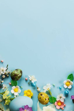 Happy Easter! Easter flat lay with stylish eggs and blooming spring flowers on blue background, space for text. Modern greeting card or banner. Natural painted colorful eggs and blossom
