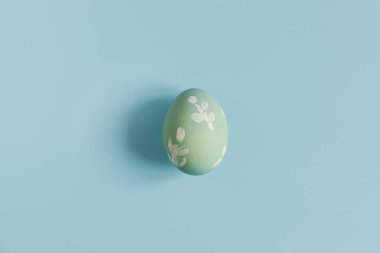 Stylish easter egg on blue background flat lay. Minimal Easter still life. Modern greeting card or banner, copy space. Happy Easter! Natural painted green egg