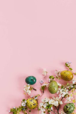 Stylish easter eggs and blooming flowers on pink background flat lay. Happy Easter! Natural painted colorful quail eggs and cherry blossom. Modern greeting card or banner, copy space
