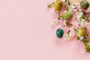 Happy Easter! Easter stylish eggs and blooming spring flowers on pink background, space for text. Modern greeting card or banner. Natural painted colorful quail eggs and cherry blossom