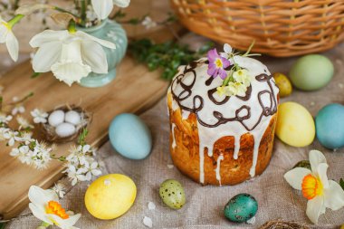 Happy Easter! Homemade easter bread and natural dyed easter eggs with spring flowers on linen napkin on rustic table. Traditional Easter food. Top view