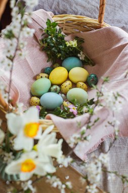 Happy Easter! Stylish natural dyed easter eggs with spring flowers on linen napkin in wicker basket. Traditional Easter food. Top view. Rustic Easter still life