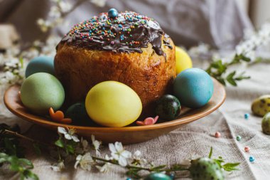 Happy Easter! Homemade easter bread and natural dyed easter eggs with spring flowers on wooden plate on rustic table. Traditional Easter food.