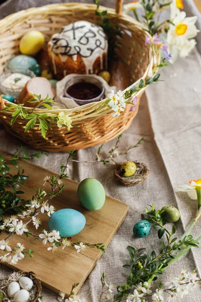 Natural dyed easter eggs on background of homemade easter bread, ham, beets, butter on rustic table with spring blossoms and linen napkin. Top view. Traditional Easter food in basket