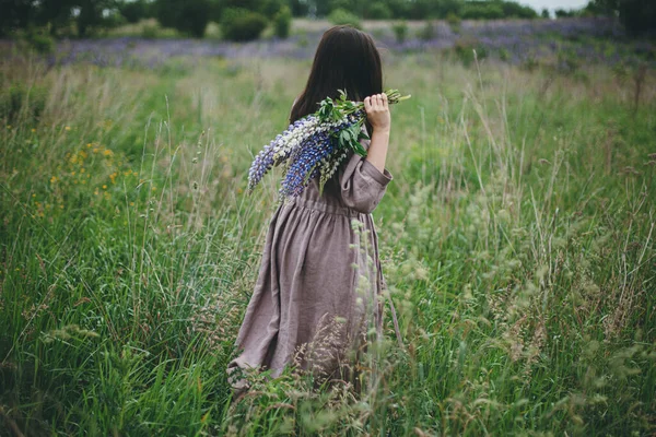 时尚的女人穿着乡村的衣服 在草地上采摘紫丁香花束 充满情调 土工布美学 穿着亚麻布衣服的年轻女子在夏天的乡间捧着野花 乡村的生活慢悠悠 — 图库照片