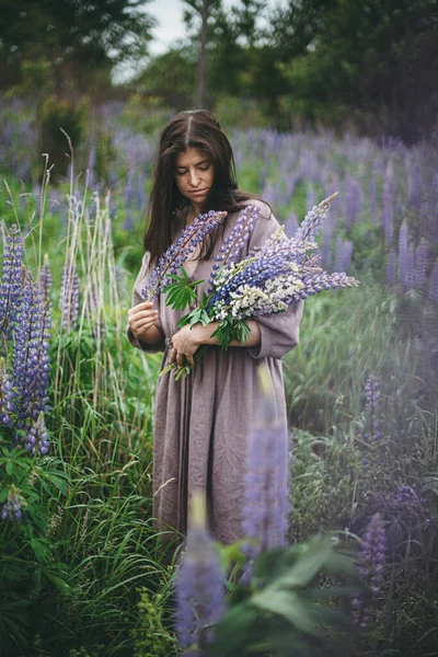 土工布美学 穿着乡村服装的时髦女人在草地上采摘丁香花 穿着亚麻布衣服的年轻女性 在夏日的乡间野花丛生 乡村生活缓慢 — 图库照片
