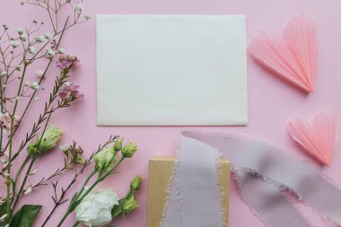Stylish empty greeting card, gift and beautiful flowers on pink background flat lay. Happy women's day and mother's day. Space for text