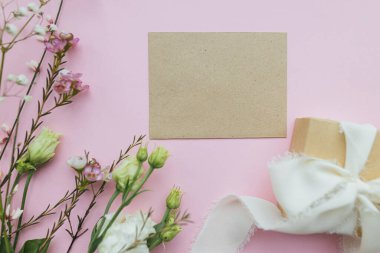 Stylish empty greeting card, gift and beautiful flowers on pink background flat lay. Happy women's day and mother's day. Space for text