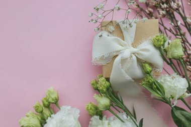 Happy womens day and mother's day concept. Stylish simple gift with ribbon and beautiful tender flowers on pink background flat lay with space for text. Floral greeting card or banner