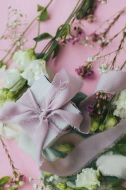 Stylish simple gift with ribbon and beautiful tender flowers on pink background flat lay. Happy womens day and mother's day concept. Floral greeting card or banner