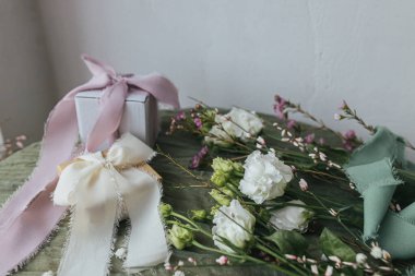 Stylish simple gift with silk ribbons and beautiful flowers on green fabric background. Happy women's day and mother's day concept. Modern spring holiday still life. Greeting card