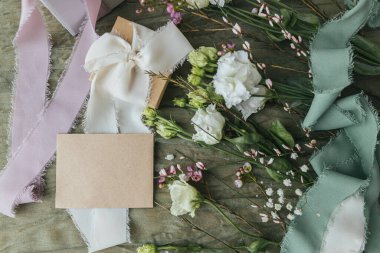 Stylish empty card, gift and beautiful flowers with ribbons on green fabric background flat lay. Happy women's day and mother's day concept. Greeting card template, space for text