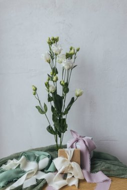Stylish simple gift with silk ribbons and modern bouquet on green fabric against rustic wall. Happy women's day and mother's day concept. Modern spring holiday still life. Greeting card