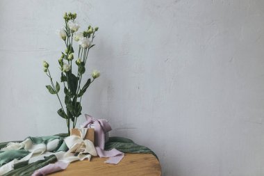 Stylish simple gift with silk ribbons and modern tender bouquet against rustic wall. Happy women's day and mother's day concept. Spring holiday still life. Greeting card, space for text
