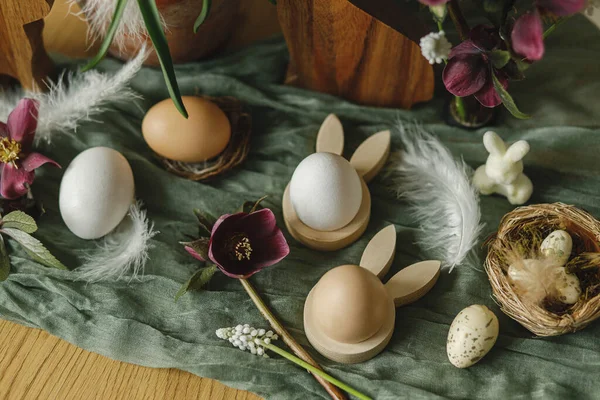 ハッピーイースター スタイリッシュな木製のウサギの耳と自然卵 春の花 羽や部屋の素朴なテーブルの上に巣 イースターはまだ生きてる 農家でのお祭りの配置と装飾 トップビュー — ストック写真