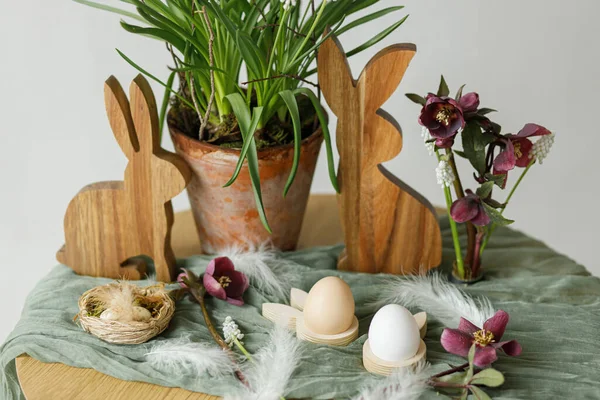 ハッピーイースター スタイリッシュな木製のウサギ 自然卵 春の植木鉢と花 部屋の素朴なテーブルの上の羽 イースターはまだ生きてる 農家でのお祭りの配置と装飾 — ストック写真