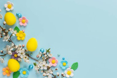Şık Paskalya yumurtaları, şeker çiçekleri ve kiraz çiçekleri mavi arka planda, fotokopi alanı ile düzleştirilmiş. Mutlu Paskalyalar! Tebrik kartı şablonu veya modern bayram afişi