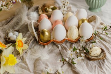 Stylish easter eggs and blooming spring flowers on rustic fabric background. Happy Easter! Rustic easter still life. Modern eggs in tray and wildflowers