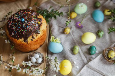 Homemade easter bread and natural dyed easter eggs with spring flowers on linen napkin on rustic table. Traditional Easter food. Top view. Happy Easter!