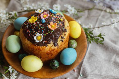 Happy Easter! Homemade easter bread and natural dyed easter eggs with spring flowers on wooden plate on rustic table. Top view. Traditional Easter food.