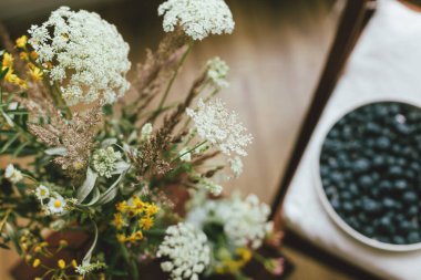 Yabanmersinlerinin arka planında kır odasındaki modern seramik tabakta yabani çiçekler. Kırsal kesimde yaz mevsimi. Sağlıklı gıda estetiği. Yaz meyveleri