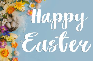 Yuvadaki şık yumurtalar, renkli çiçekler ve kiraz çiçekleri üzerine Mutlu Paskalya yazıları mavi arka planda yatıyordu. Modern Paskalya tebrik kartı. El yazısıyla yazılmış harfler