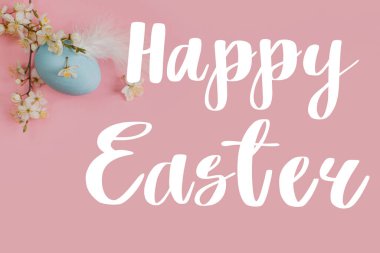 Mutlu Paskalya tebrik kartları. Mavi Paskalya yumurtası ve pembe arka planda kiraz çiçeği üzerine Mutlu Paskalya metinleri. Modern tebrik kartı. El yazısı işareti