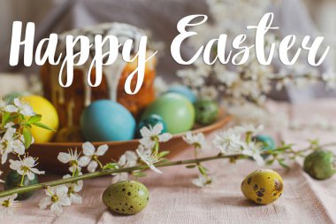 Doğal boyalı yumurtalar, bahar çiçekleri ve kırsal masada paskalya pastası üzerine Mutlu Paskalya tabelası. Modern Paskalya tebrik kartı. El yazısıyla yazılmış harfler