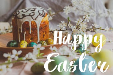 Paskalya pastası ve kır masasındaki ahşap tabakta bahar çiçekleri olan doğal boyalı yumurtalar üzerine Mutlu Paskalya yazıları. Modern Paskalya tebrik kartı. El yazısıyla yazılmış harfler