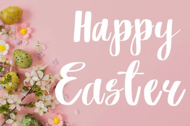 Paskalya yumurtaları ve pembe arka planda açan kiraz çiçekleri üzerine Mutlu Paskalya tabelası. Modern Paskalya tebrik kartı. El yazısıyla yazılmış harfler