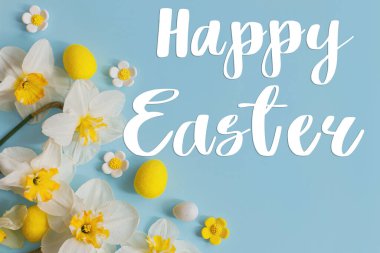 Mutlu Paskalya tebrik kartları. Paskalya yumurtaları ve sarı nergis çiçekleri üzerine Mutlu Paskalya metinleri mavi arka planda yatıyordu. Modern tebrik kartı. El yazısı işareti