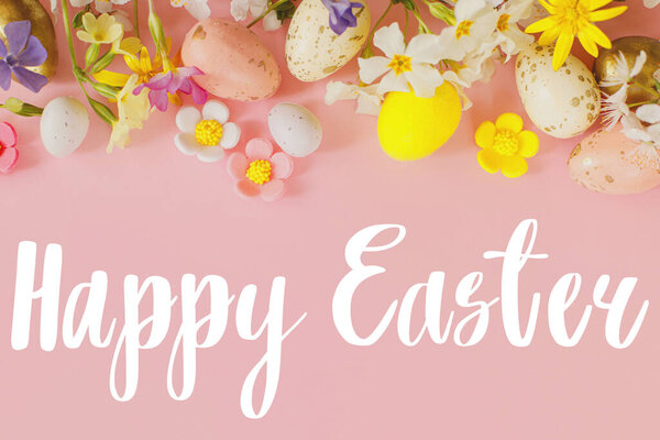 Happy Easter text sign on stylish eggs and blooming flowers on pink background flat lay. Modern Easter greeting card. Handwritten lettering