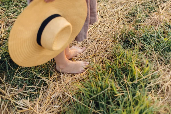 头戴帽子的女人赤脚走在落日下的稻草地里 关门了 农村缓慢的生活 大气宁静的时刻 夏乡的年轻女子穿着淡雅的亚麻布衣服 — 图库照片