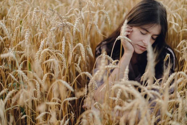 夕方の光の中で小麦畑に座っているスタイリッシュな穏やかな女性 落ち着いた雰囲気の瞬間 夏の夜の田舎でリラックスした素朴なリネンのドレスの若い女性 農村のスローライフ — ストック写真