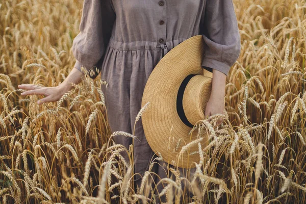 麦畑に小麦粉の茎を保持わら帽子を持つ女性 クロップドビュー 落ち着いた雰囲気の瞬間 田舎の夏に熟した小麦の耳に触れる素朴なリネンのドレスの女性 農村のスローライフ — ストック写真
