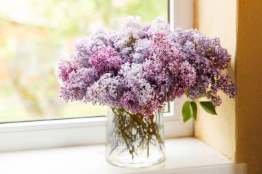 Güneşli odada pencere kenarında güzel leylak çiçekleri. Çiçekli yazlık ev dekoru. Kırsal evdeki vazoda pembe ve mor leylaklar.