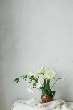 Anneler Günün kutlu olsun. Güzel beyaz laleler ve eski vazodaki nergisler ahşap masada, kırsal duvarın karşısında. Basit bahar buketi, çiçekli natürmort. Kadınlar Günü 'nde. Metin için boşluk
